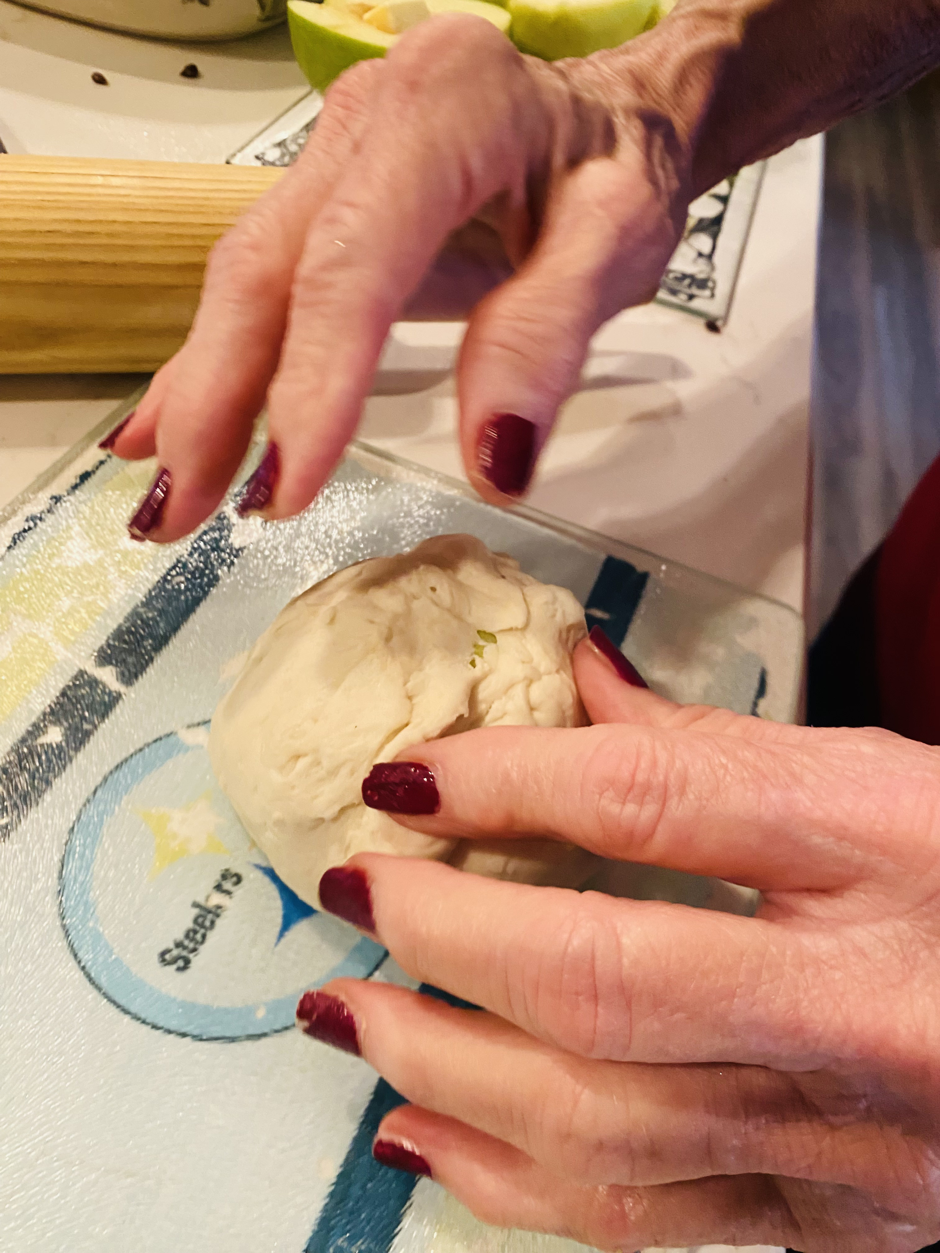 Two pairs of hands preparing an apple in a kitchen.