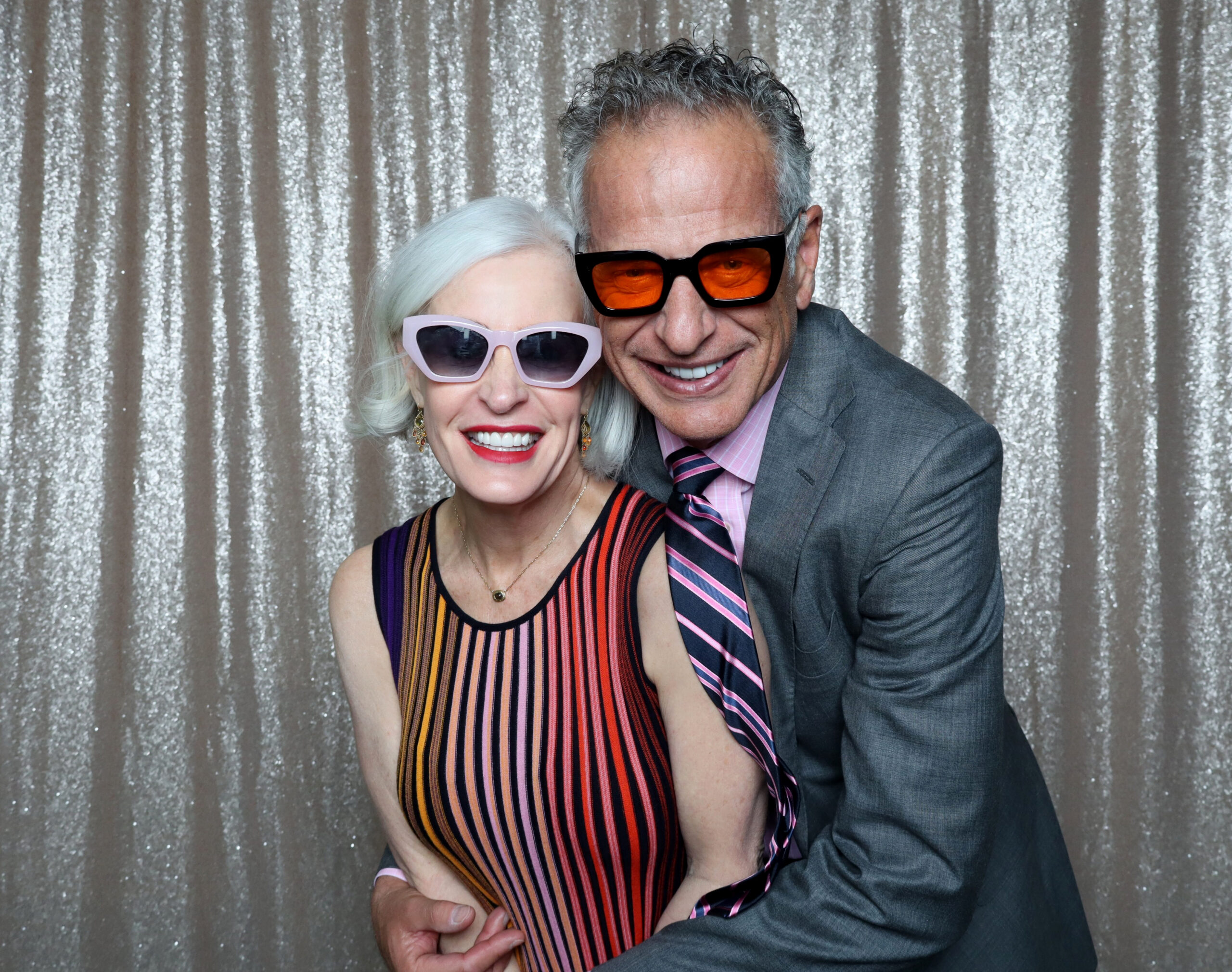 Celebration guests enjoying props in front of a silver sequin backdrop