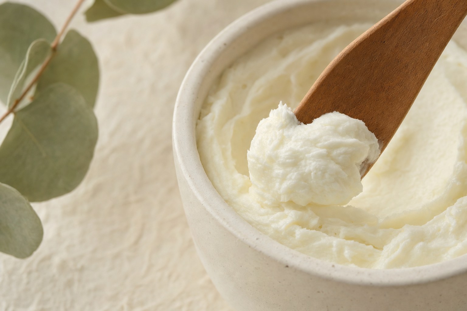 A wooden scoop lifting rich body butter from a ceramic bowl