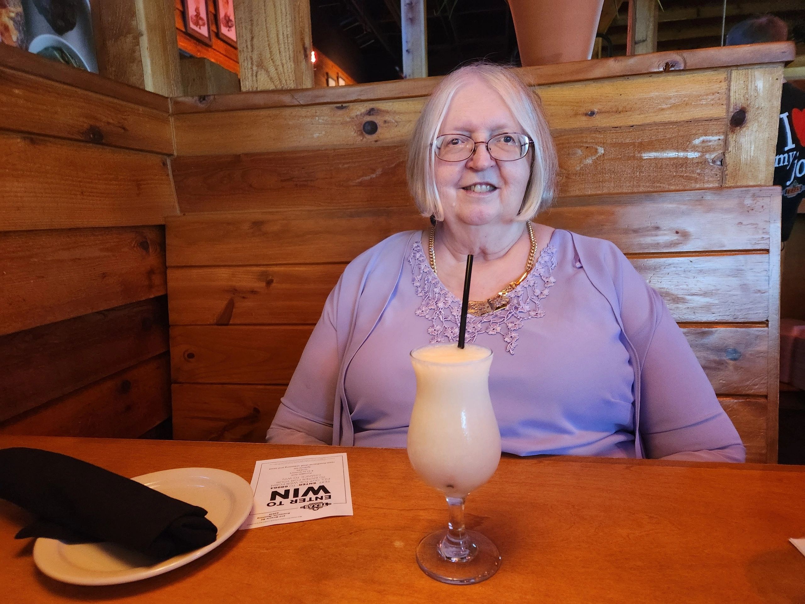 Teressa L. Diggs in a purple dress, seated at a table with a pina colada