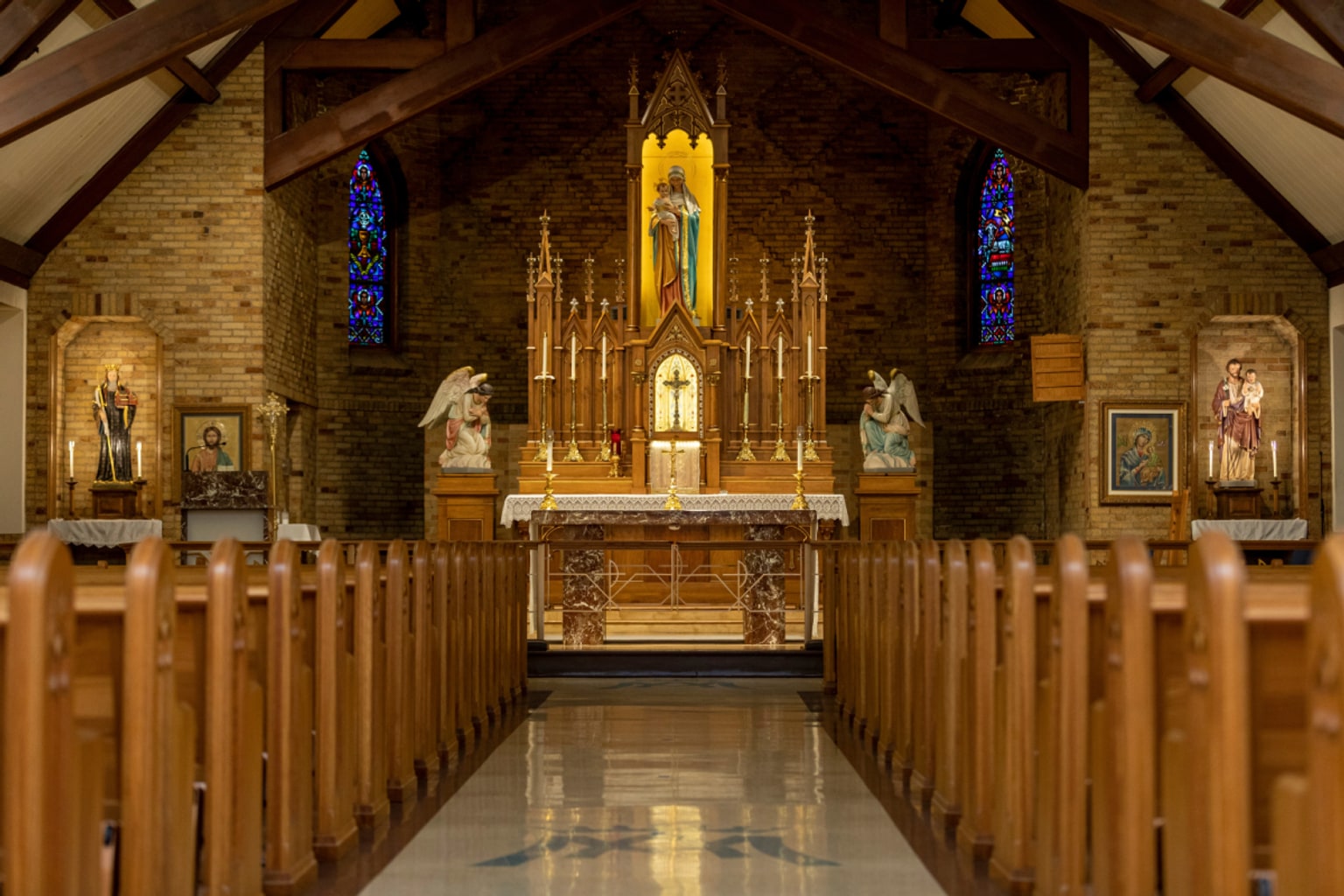 Quiet Catholic chapel with wooden pews leading toward a softly lit altar