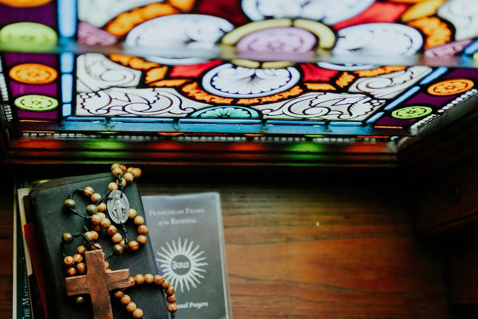 Rosary resting on a prayer book beside a stained-glass window
