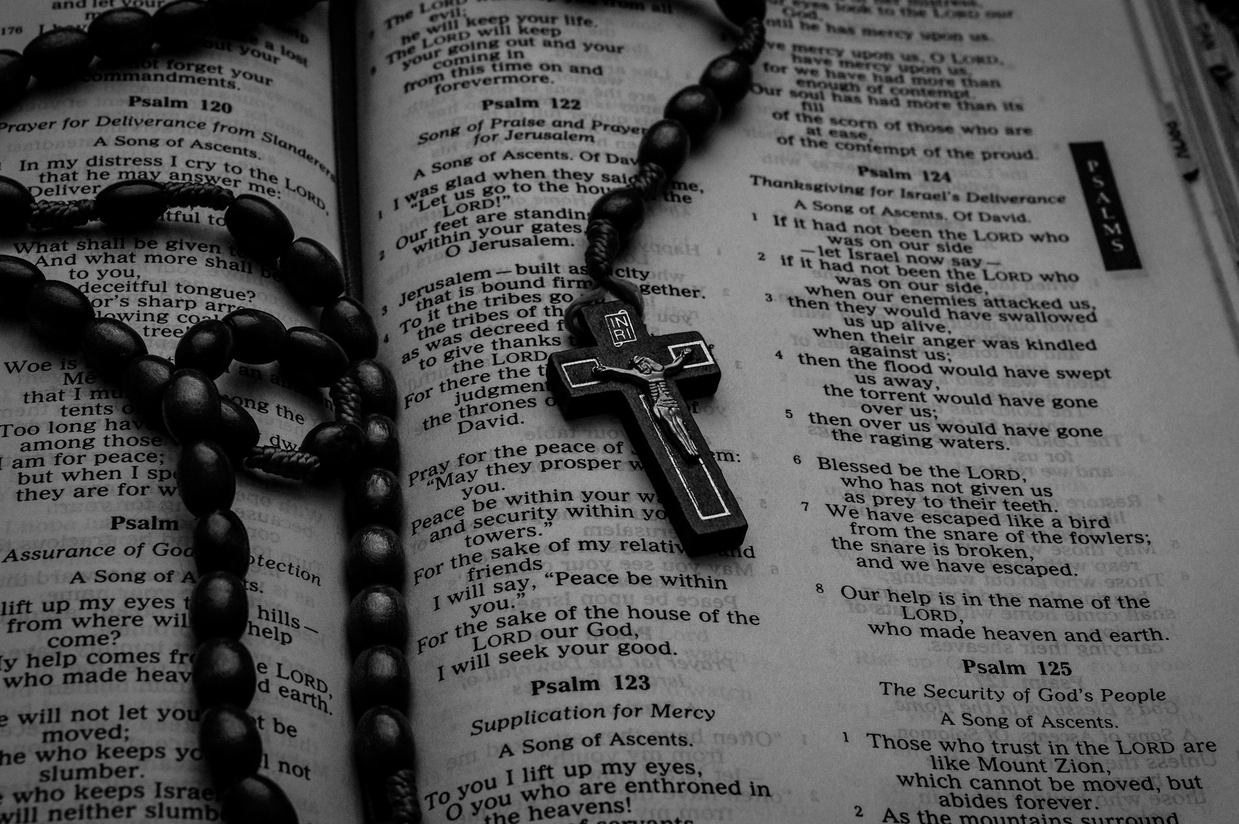 A dark wooden rosary and crucifix resting on an open Bible