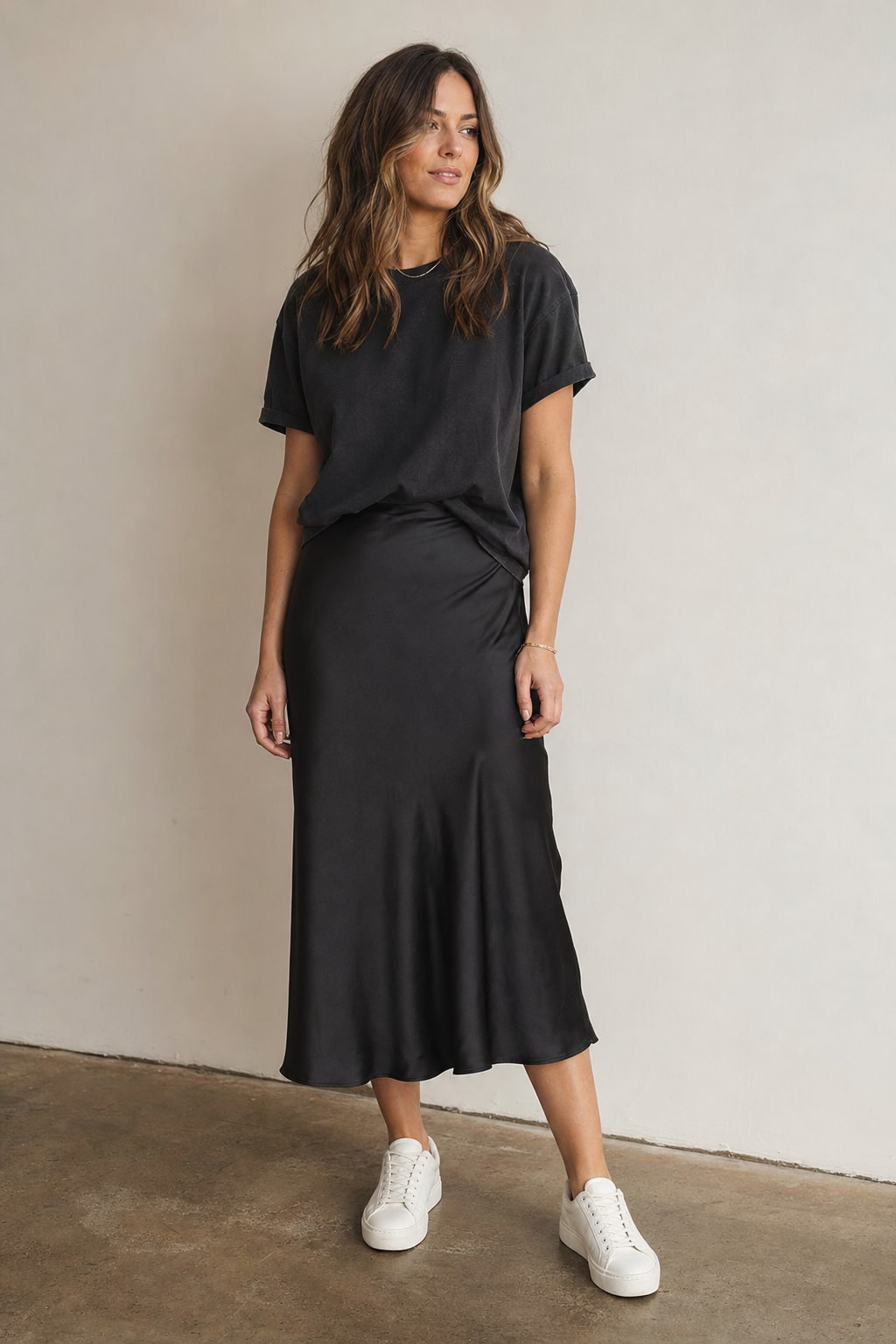 Woman in a charcoal T-shirt, black satin midi skirt, and white sneakers