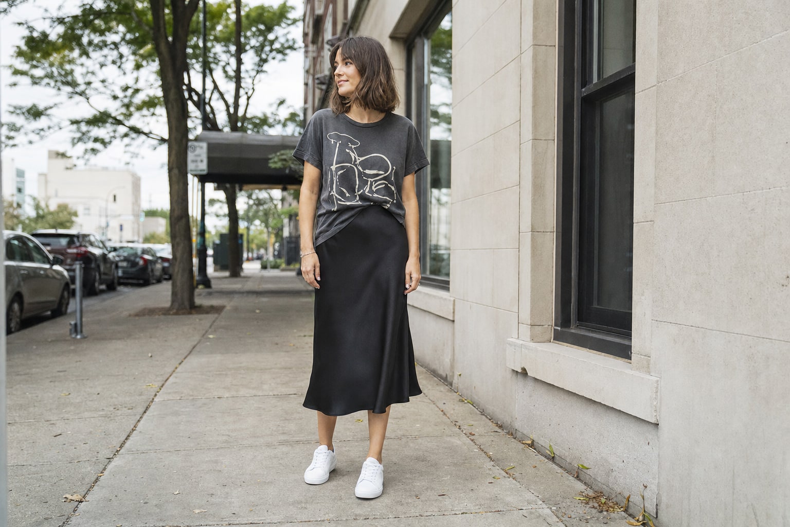Charcoal graphic T-shirt tucked into a black satin midi skirt with white sneakers