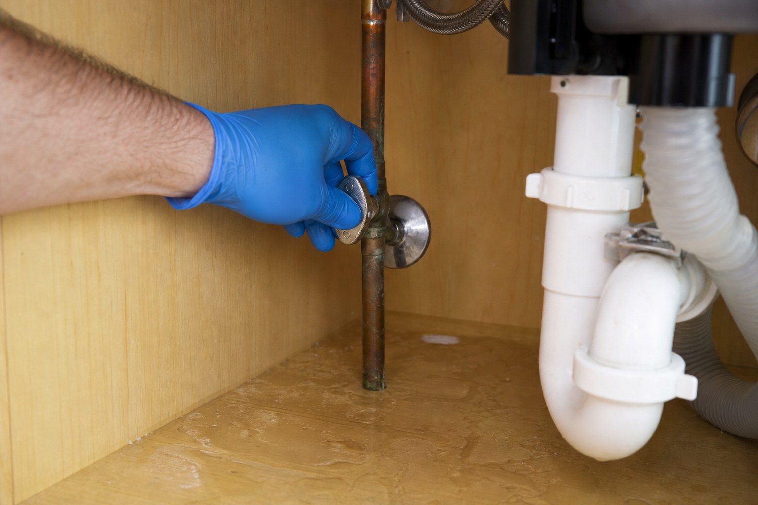 Gloved hand turning off a water supply valve below a sink
