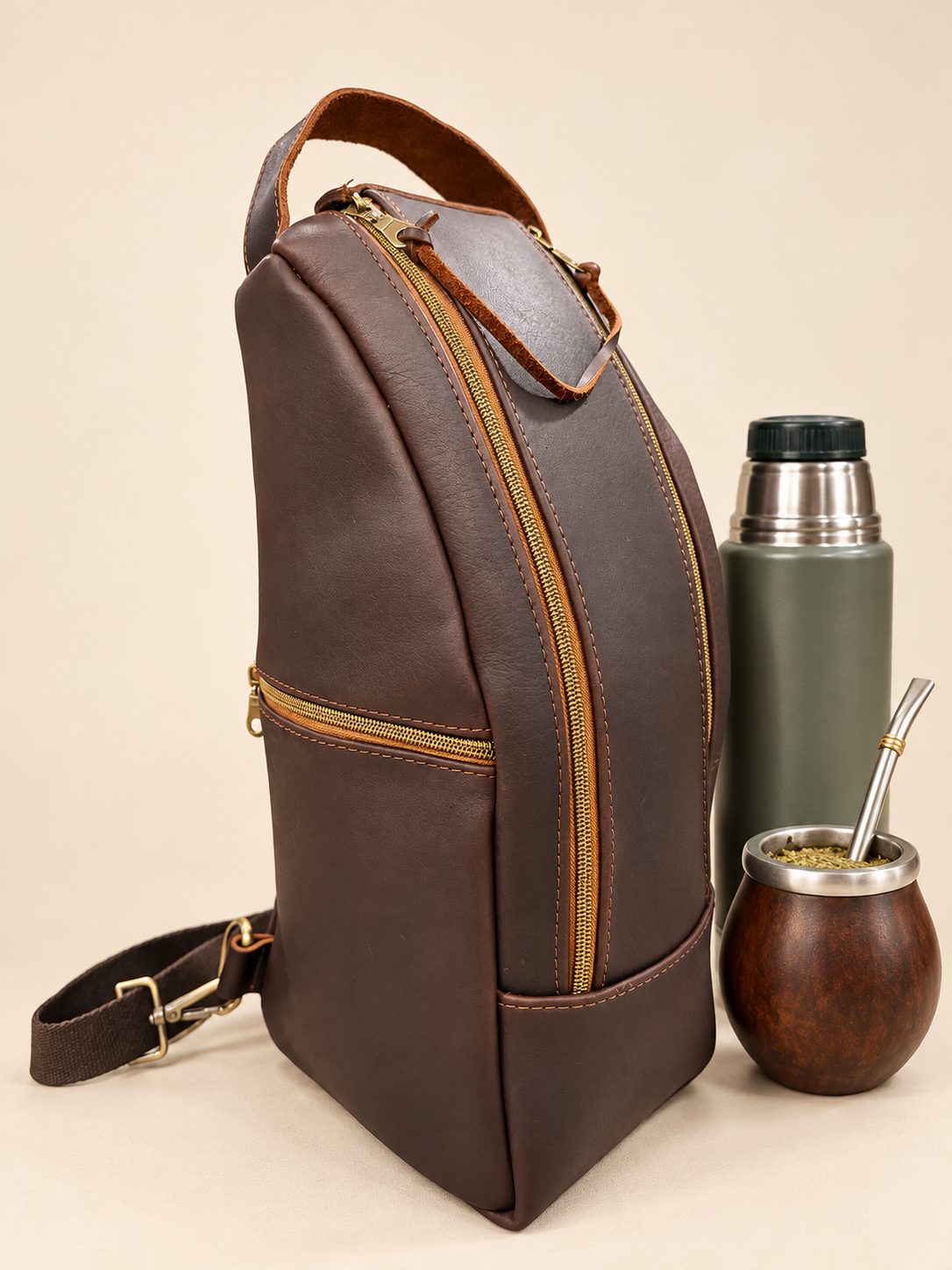 Handmade brown leather mate bag with golden zippers beside a green thermos and wooden mate