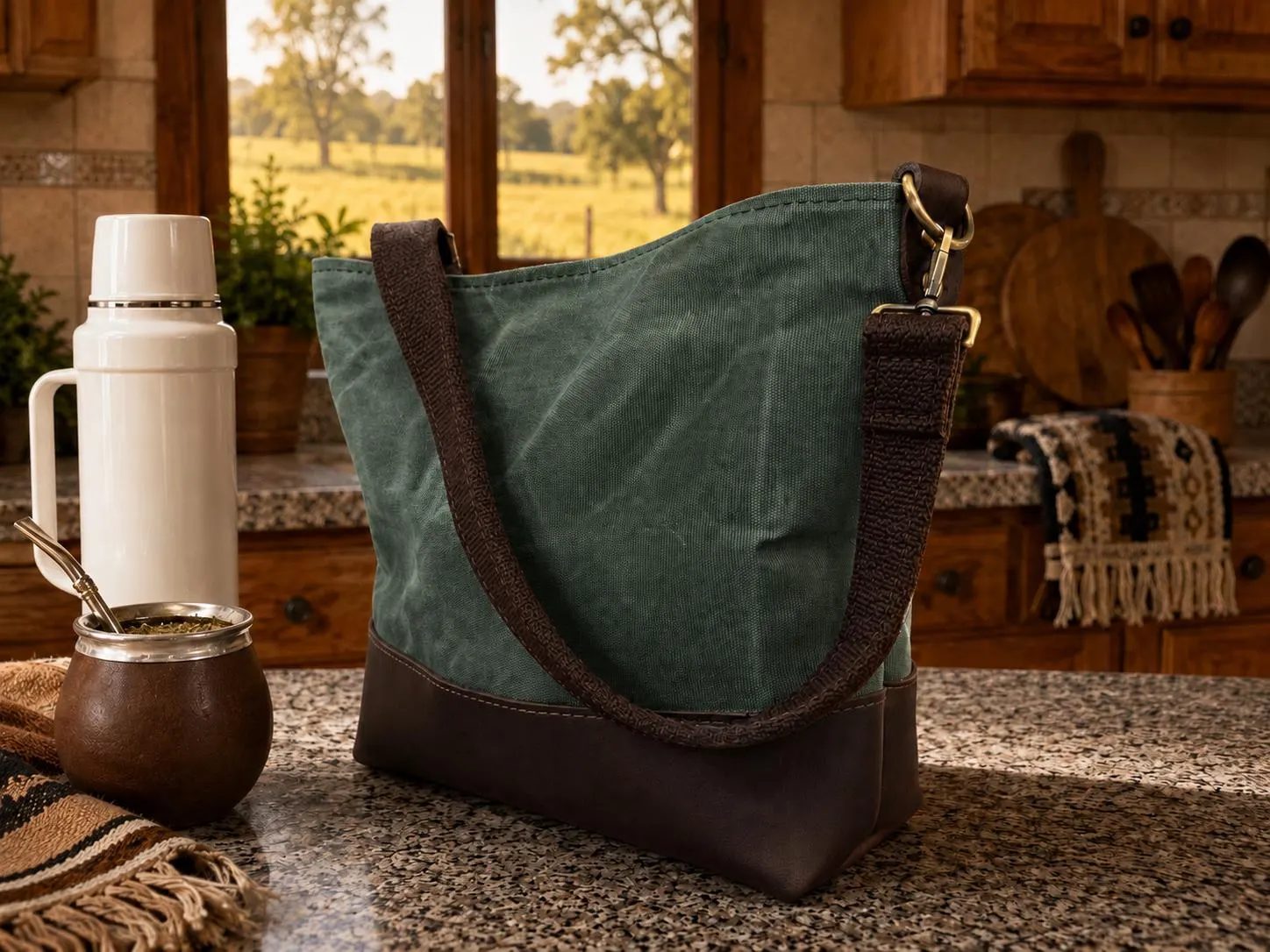 Green canvas mate bag with dark leather base and strap, beside a thermos and mate
