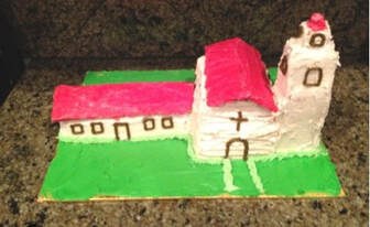 A handcrafted model of a church with a red roof and white walls.