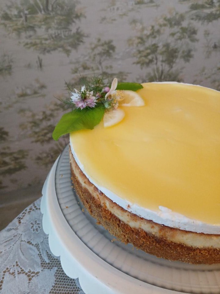 A lemon-glazed cheesecake with a flower and leaf garnish.
