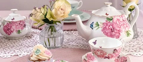 Elegant tea set with floral patterns and fresh roses on a lace tablecloth.