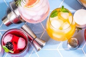 Colorful cocktails with ice and garnishes on a blue tiled surface.