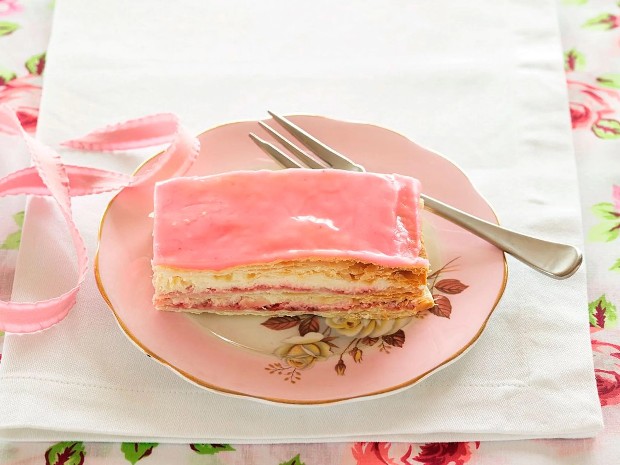 A slice of layered pink frosted cake on a pink plate.