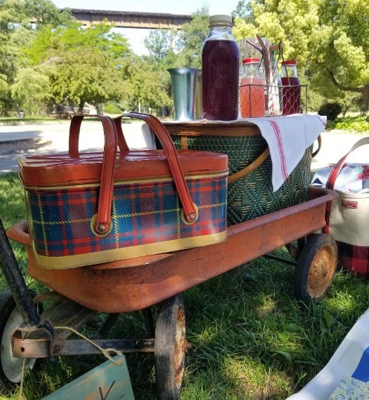 Vintage wooden picnic basket with plaid pattern on a green table outdoors.