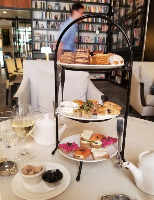 Elegant three-tiered afternoon tea with sandwiches, pastries, and a glass of white wine.