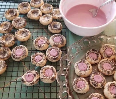 Mini tartlets with pink icing and decorative centers on cooling racks.