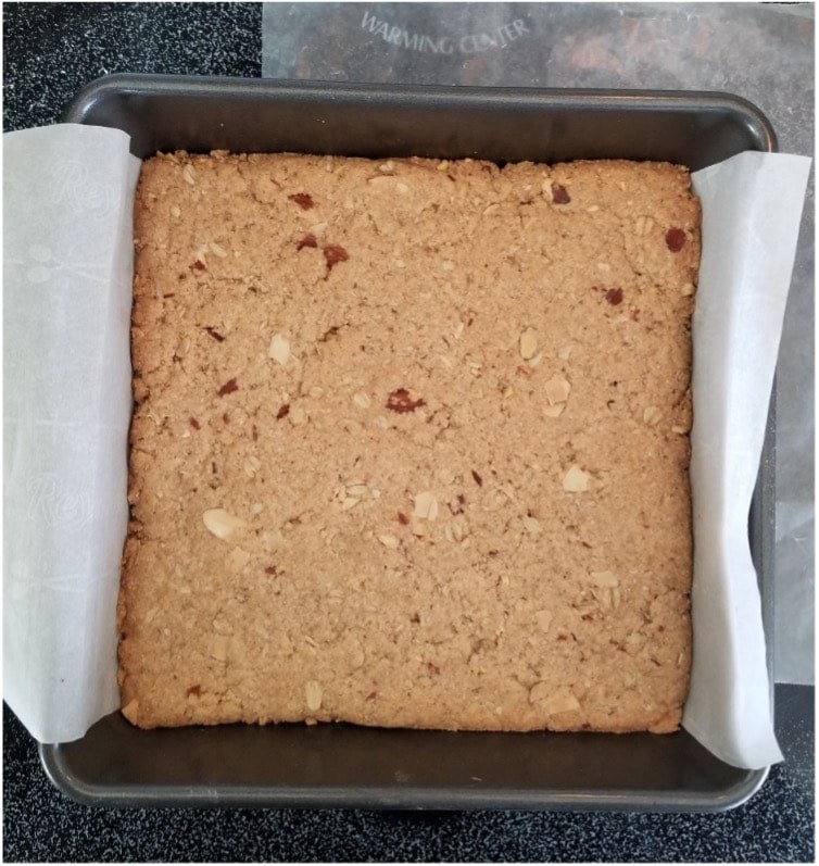 Square tray of freshly baked nutty blondies lined with parchment paper.