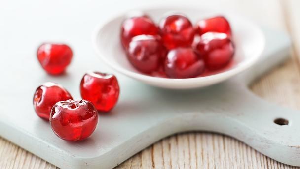 Bright red cherries placed on a wooden surface and in a white bowl.