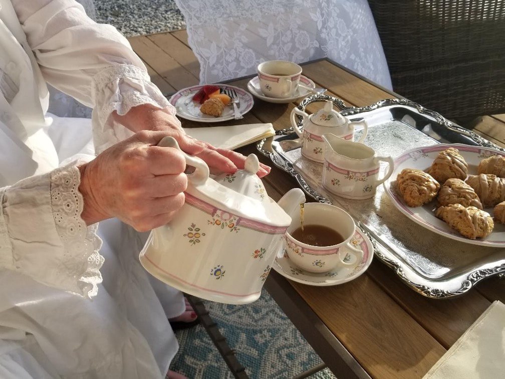 Person pouring tea from a floral teapot into a cup at a cozy table.