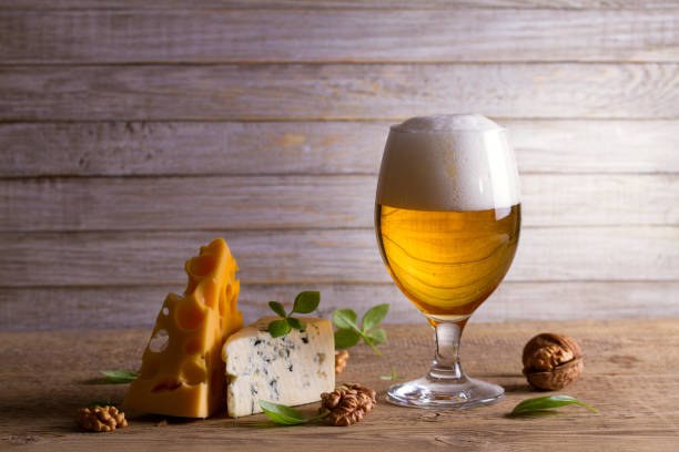 A glass of beer with cheese and walnuts on a wooden table.