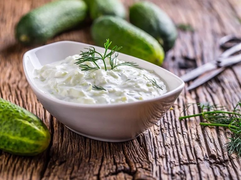 A bowl of creamy tzatziki sauce garnished with dill on a wooden table.