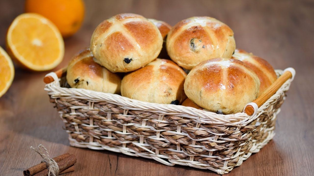 Fresh hot cross buns with raisins in a woven basket.