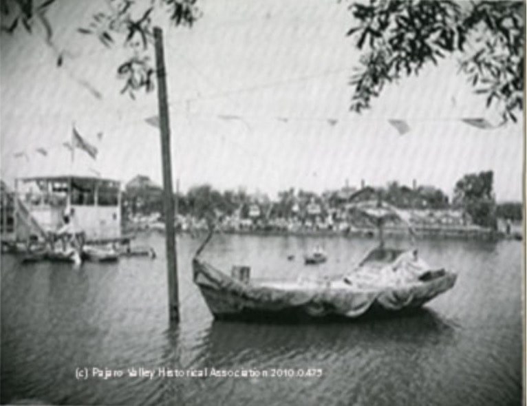 Vintage boat docked by the riverside with a village in the background.