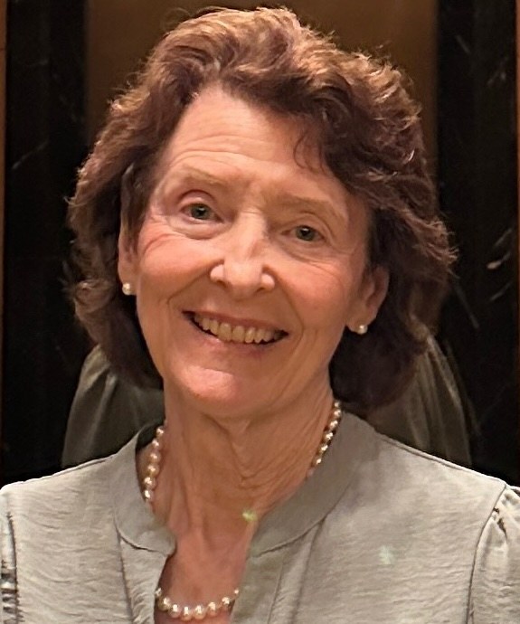Smiling elderly woman with pearl necklace and light gray outfit.