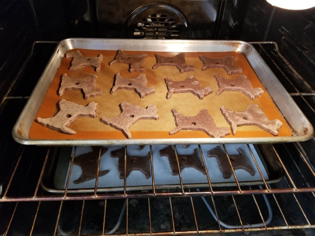 Dog-shaped cookies baking on a tray in the oven.