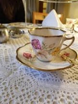 Elegant porcelain teacup and saucer with floral design on lace tablecloth.