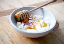 Bowl of yogurt drizzled with honey and a honey dipper.