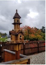 Handcrafted wooden birdhouse with multiple compartments under cloudy skies.