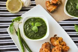 A bowl of green chutney with fried snacks and green chili on the side.