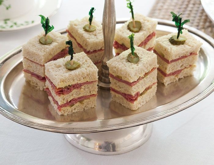 Layered finger sandwiches with herb garnish on a silver tray.