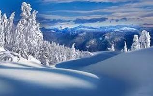 Snow-covered landscape with frosted trees and distant mountains under a blue sky.