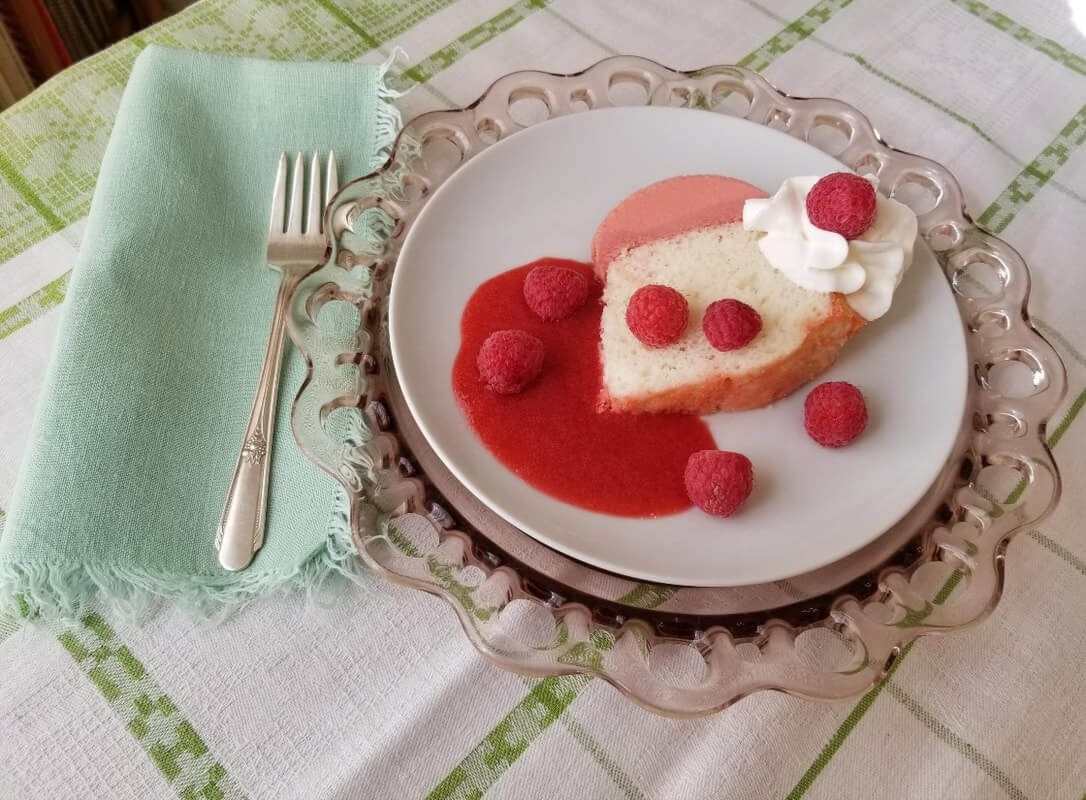 A heart-shaped cheesecake with raspberry sauce and fresh raspberries on a decorative plate.