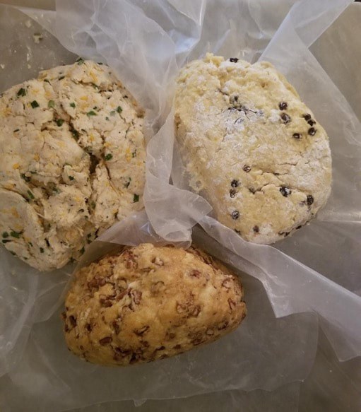 Three freshly baked scones with different ingredients on parchment paper.