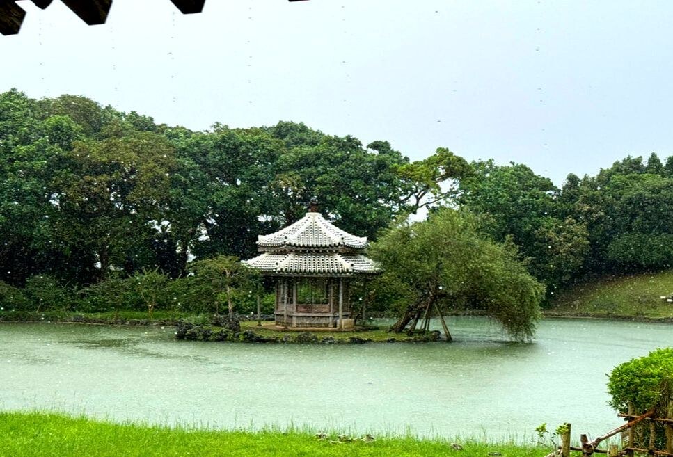 A serene gazebo on an island in a pond surrounded by greenery.