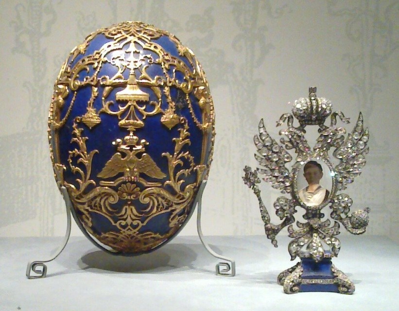 A richly decorated blue and gold Fabergé egg with a jeweled figurine.