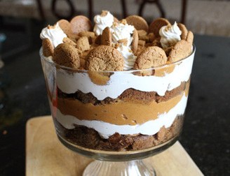 Layered pumpkin dessert with whipped cream and cookies in a glass bowl.
