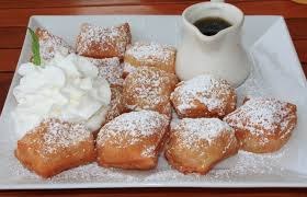 Beignets dusted with powdered sugar served with coffee and whipped cream.