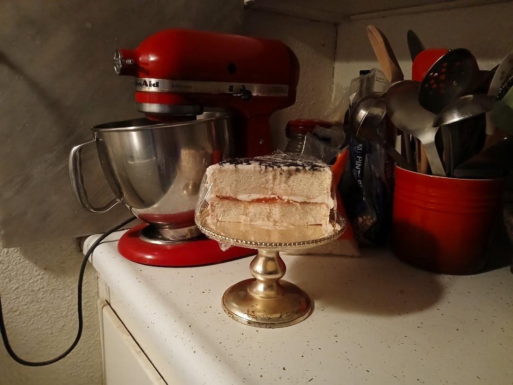 A layered cake with cream on a gold stand in a cozy kitchen.