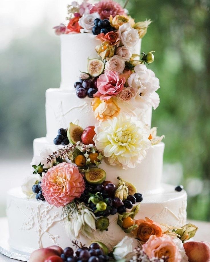 Elegant white wedding cake adorned with cascading fresh flowers in soft pastel hues.
