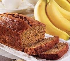 Freshly baked banana bread with sliced pieces and bananas in the background.