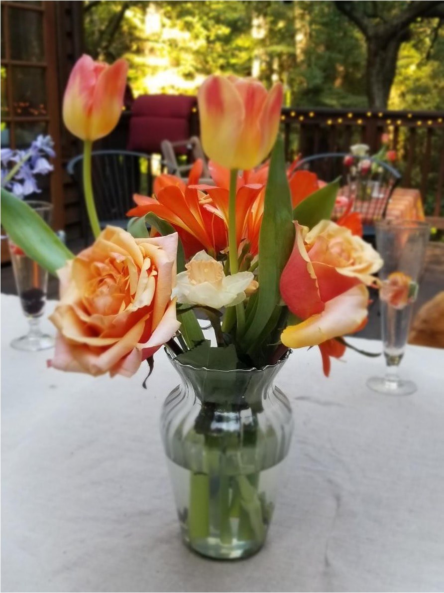A small bouquet of orange and peach roses in a glass vase on a table.