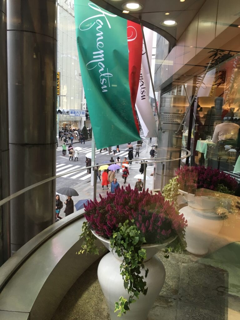 View from a café window showing flowers and a busy street.