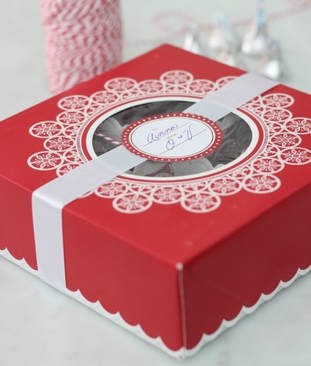 A red gift box with intricate white lace design and a circular label.