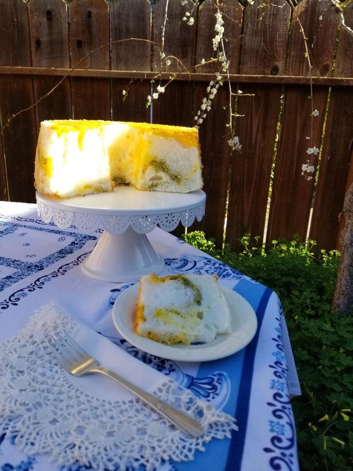 A colorful mango and cream dessert cake on a white stand outdoors.
