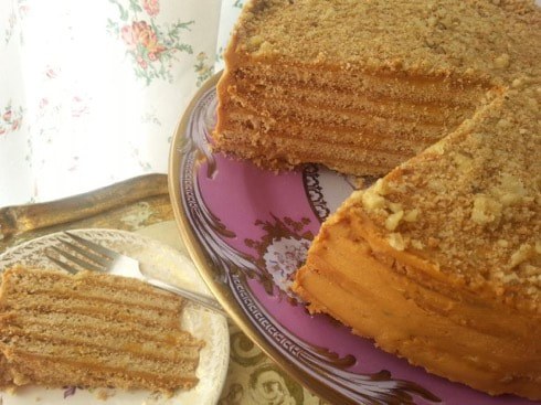 A layered honey cake on a decorative plate with a slice served on a saucer.