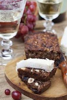 A slice of nut-studded cake with white topping on a wooden board.